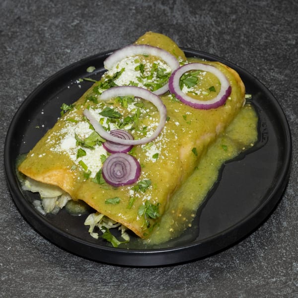 Two green enchiladas topped with red onion, cotija cheese, and cilantro on a black plate.