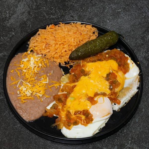 Huevos Rancheros with refried beans, rice, and a green chile on a black plate.