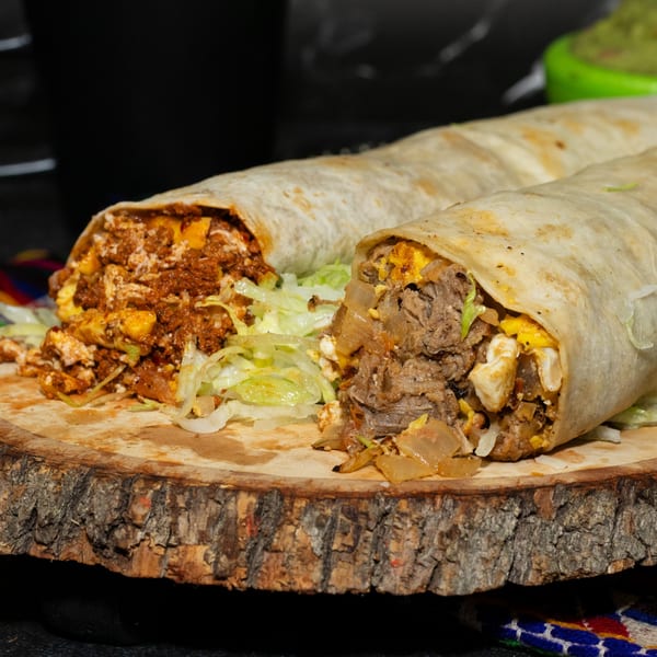 Two large, cut burritos overflowing with meat, cheese, and lettuce on a wooden board.