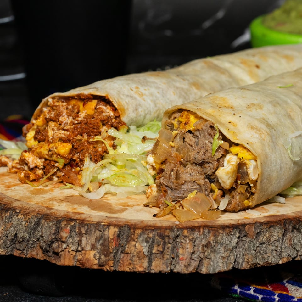 Two large, cut burritos overflowing with meat, cheese, and lettuce on a wooden board.