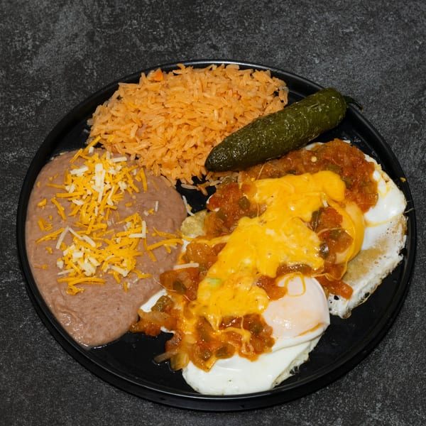 Huevos Rancheros with rice, refried beans, and a whole jalapeño on a black plate.