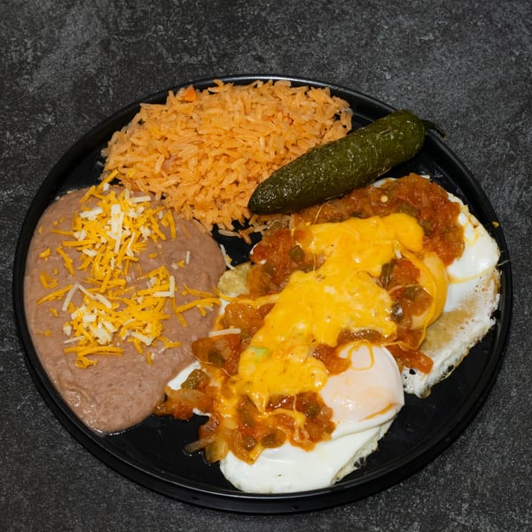 Huevos Rancheros with refried beans, Mexican rice, and a green chili on a black plate.