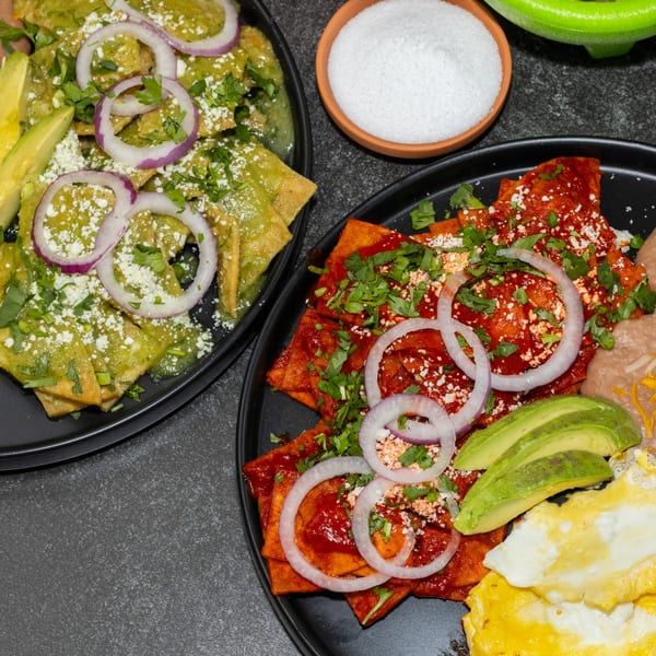 Two plates of chilaquiles, one green and one red, with avocado, onions, and cheese.